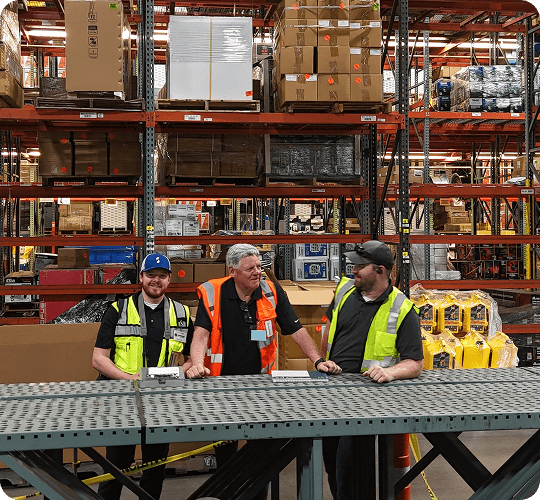 Three workers discussing in warehouse setting.