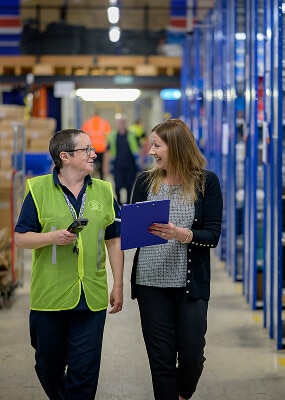 Two people discussing in warehouse aisle.
