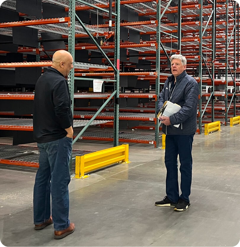 Two men discussing in warehouse aisle.